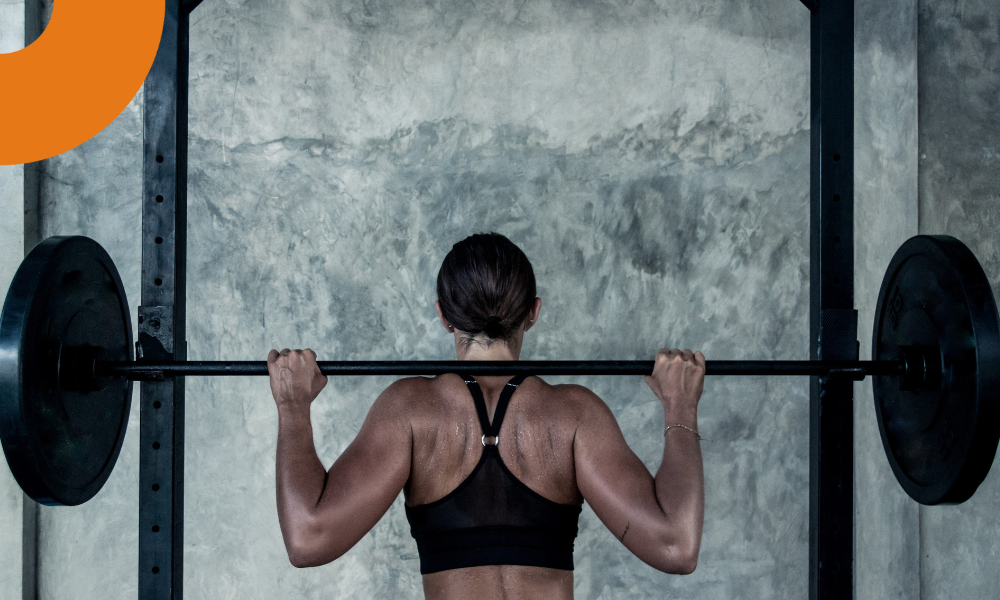 Mulher agachando no power rack da academia, estando de costas
